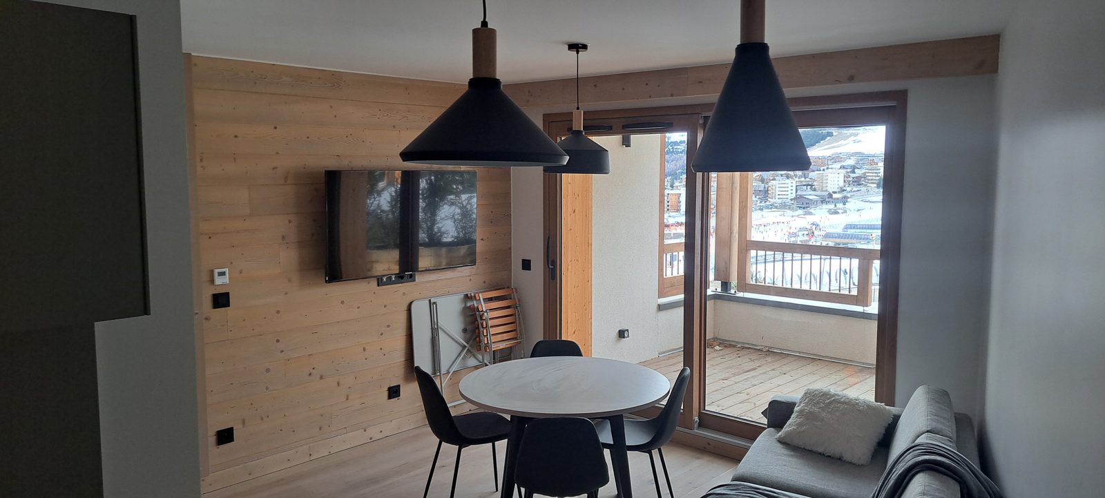 Séjour d'appartement de montagne aménagé : habillage mural bois, suspensions, coin repas et accès balcon